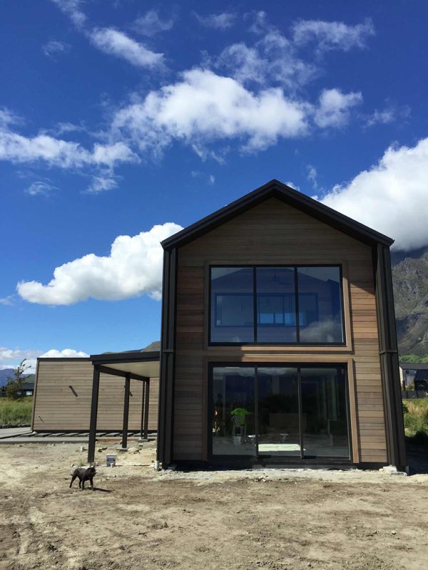 Two-storey dark timber-clad home with a gable roofline below the mountains