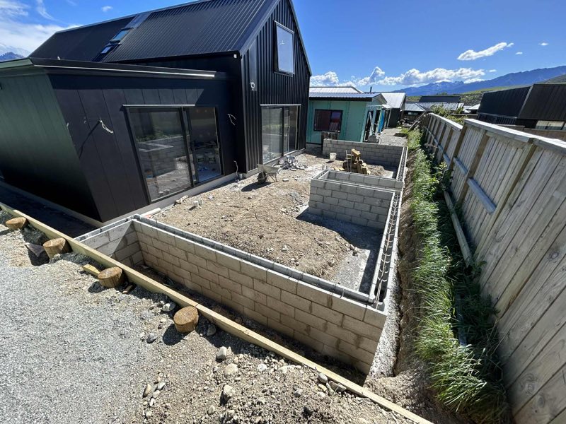 Concrete block retaining wall under construction beside a dark-clad house