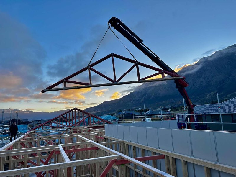 Roof truss lifted into place by crane at dusk